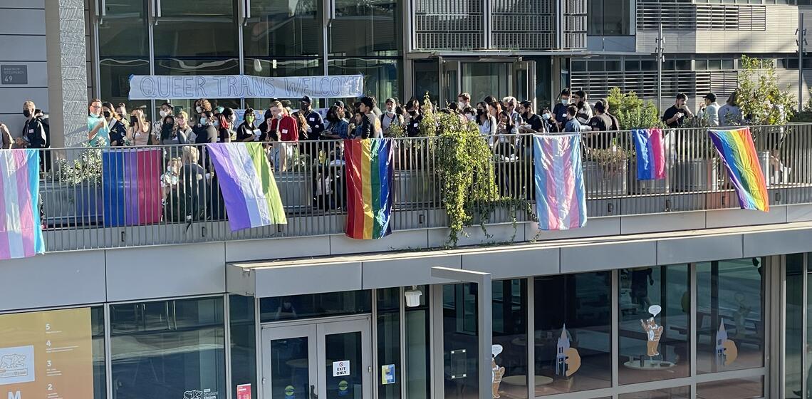 Students standing on the balcony of Cesar Chavez that has various pride flags on it.