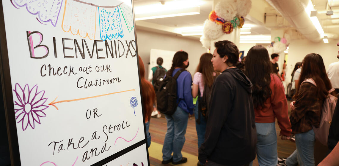 "Bienvenidxs" written on a whiteboard to the left with students walking around on the right.