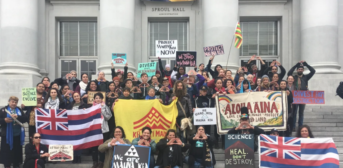 A group of about 70 PI people and allies posing in front of Sproul with signs, banners and other items supporting Mauna Kea