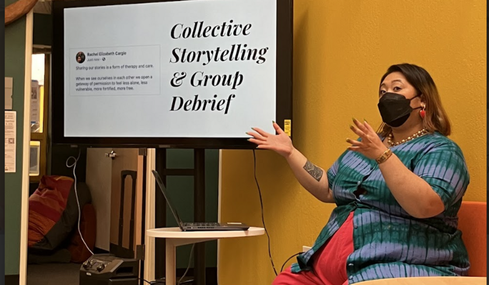 Photo of Nyingv Jae seated with screen reading "Collective Storytelling Debrief"