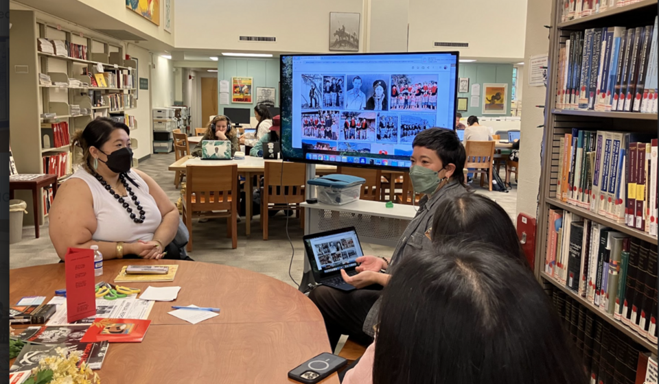 Group of people in the Ethnic Studies Libary around a TV monitor listening to presentation